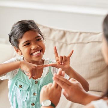 Young child communicating in sign language to another person while sitting on a couch
