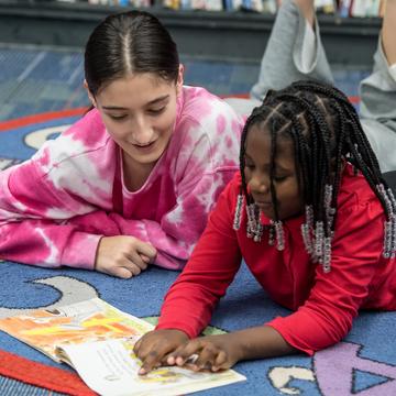 Student reading a book with an elementary student in a classroom