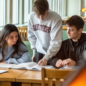 Three students studying a textbook together in a library