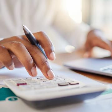 Person typing on a calculator while holding a pen