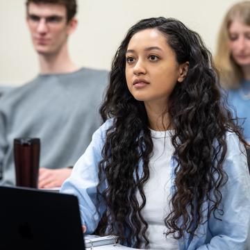 Female student sitting in a classroom with a laptop listening to a professor