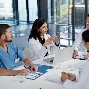 Woman sitting at a table with laptop talking to a group of people wearing scrubs