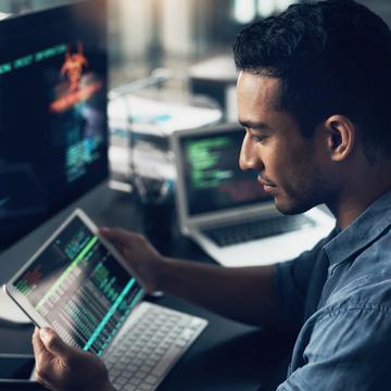 Person holding a tablet while sitting in front of a computer