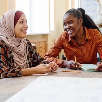 Two women sitting at a table talking with a book open in front of them