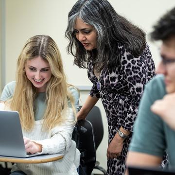 Student looking at a laptop with a professor in the classroom