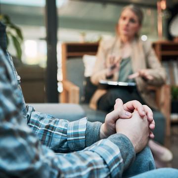 Person sitting with hands folded while talking to a therapist sitting in the background