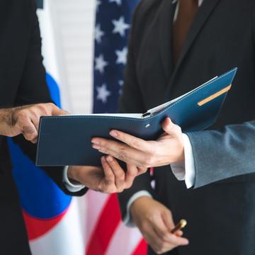 Two diplomats holding a book with international flags behind them