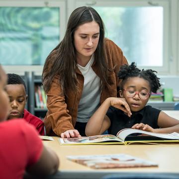 Student teacher helping young elementary school children learn how to read in a classroom