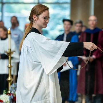 Student in a robe leading prayer at mass in a chapel