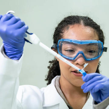 Pharmacy student wearing goggles working with dropper in lab