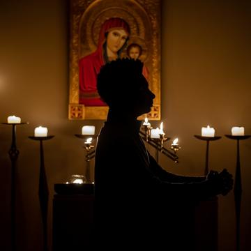 Student praying in a chapel in front of lit candles and a painting of Mary
