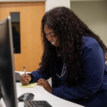 Student writing while working at a computer in the nursing station
