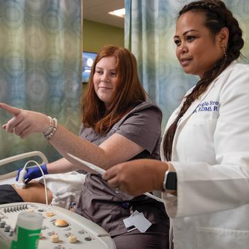 Cardiac sonography student conducting a scan on a patient with a faculty member pointing at a screen