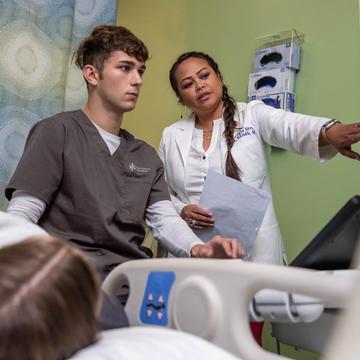 Cardiac sonography student conducting a scan on a patient with a faculty member pointing at a screen