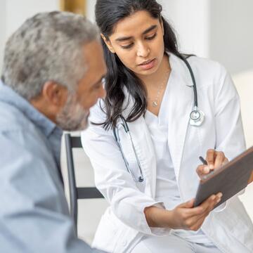 Nurse wearing a white lab coat and stethoscope pointing to a clipboard and explaining results to a patient