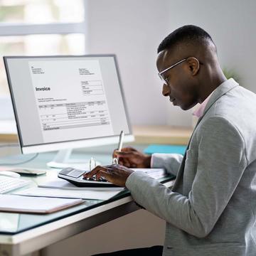 Accountant typing on a calculator while sitting in front of a desktop computer