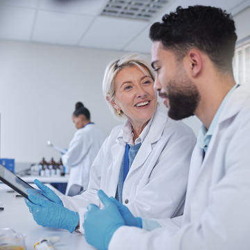 Two biotech professionals wearing lab coats looking at tablet in lab
