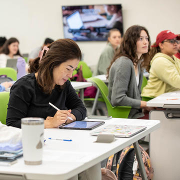 Female student writing on tablet in class