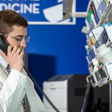 Pharmacy student on phone in front of wall of medicine