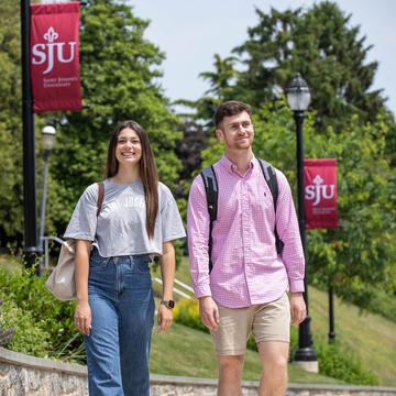 Two Saint Joseph's students walking outside with SJU banner posts behind them