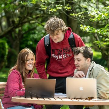 three students sitting at table looking at laptop