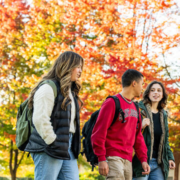 three students walking outside with fall trees around them
