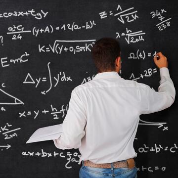 Male student writing physics equations on chalkboard