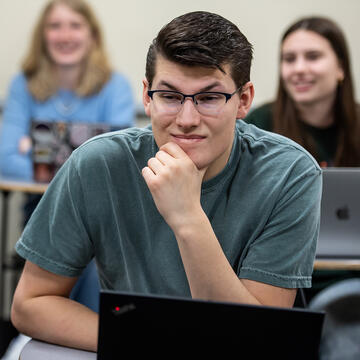 Student in classroom looking over laptop at teacher
