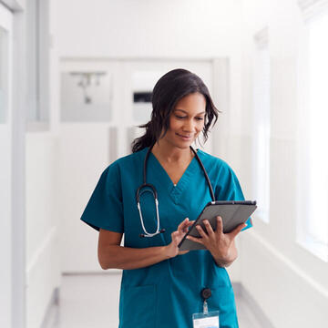 A woman in blue medical scrubs looking at a tablet computer