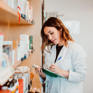 female pharmacist taking stock of bottles of pills on shelves