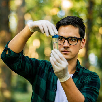male student outdoors looking at a sample test tube