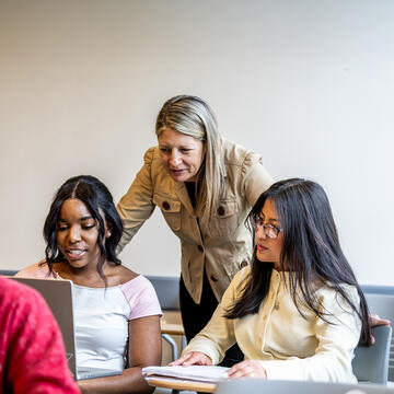 teacher leaning over two students in classroom