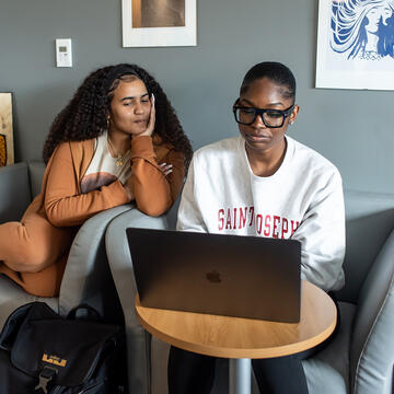 two seated students looking at laptop
