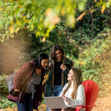 group of girls in the woods talking, one sitting and tywo standing