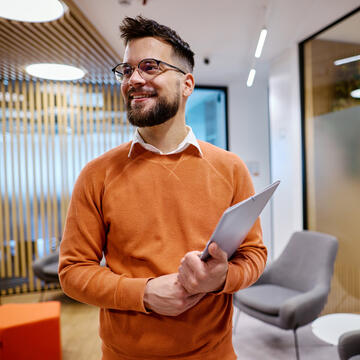 manager standing in office in an orange sweater holding a folder