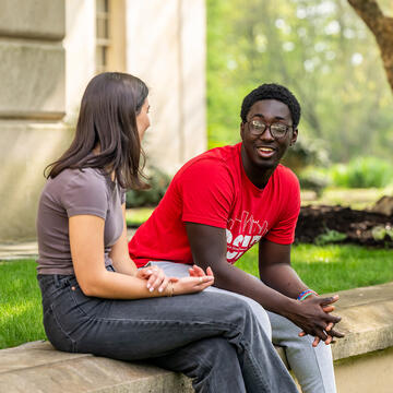 A male and female student sitting on a curb outside talking