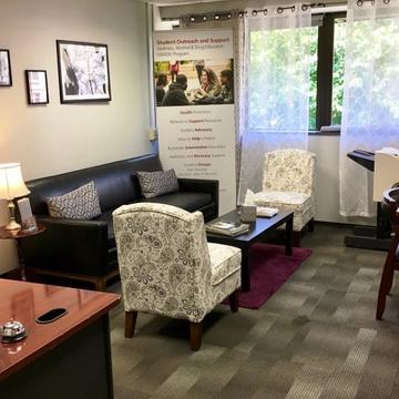 Student outreach office with two white paisley printed chairs and leather sofa around a coffee table.