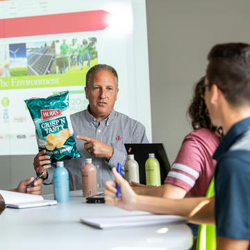 Professor holding a potato chip bag and cans of food while teaching students