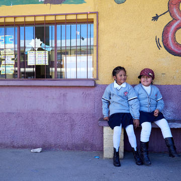 Two students sitting on a bench outside of a Bolivian school