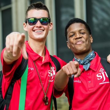 Two students smiling and pointing at the camera.