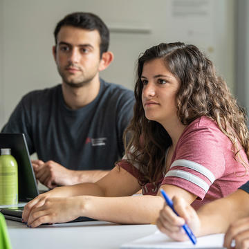 a female student wearing a red shirt and a male student wearing a gray shirt sitting inside a classroom