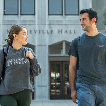 two students walking and talking right outside of a gray building