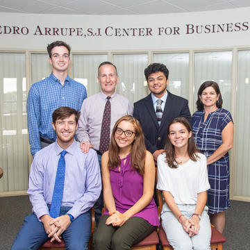 A group of students and faculty smile in front of the arrupe sign