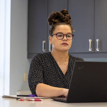 Colleen, an adult student sits at a laptop wearing glasses.
