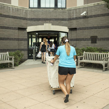 student pushing a luggage cart outside a dorm