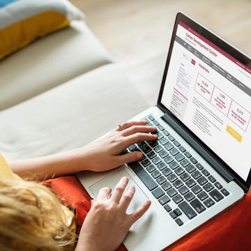 A woman sits on a couch with her laptop open. The laptop is displaying SJU's Career Development Center website.