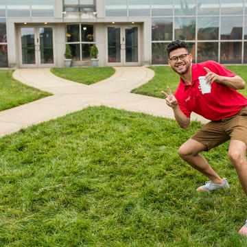 A student orientation leaders stands in front of the chapel giving a thumbs up.
