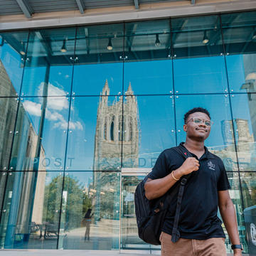 A student walks in front of the post learning commons with the reflection of barbelin behind him