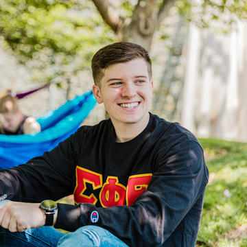 A young man with greek letters on his shirt sits in the quad
