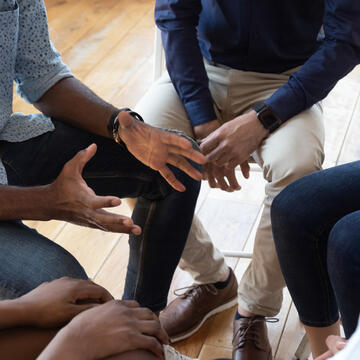 A closeup of hands in a circle, perhaps in a recovery group meeting